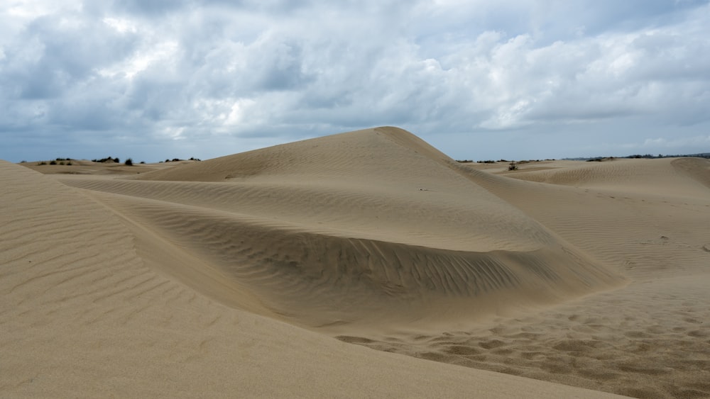 a large sand dune with a few clouds in the sky