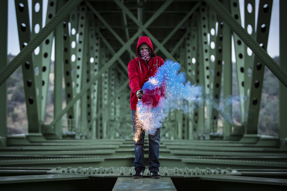 a man standing on a bridge holding a blue and red object