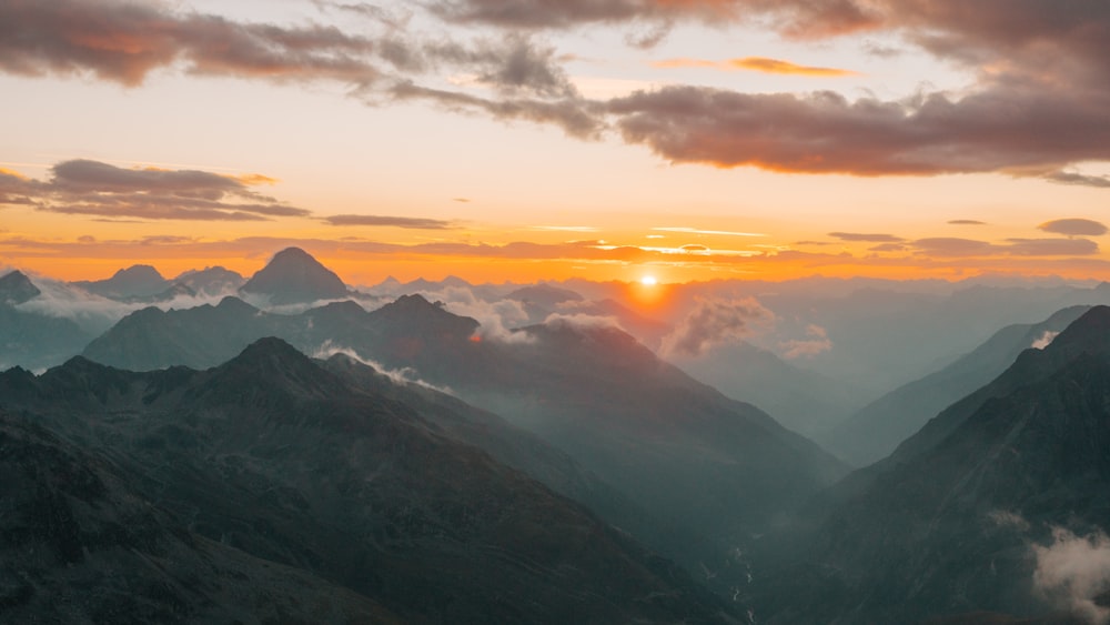 the sun is setting over the mountains and clouds