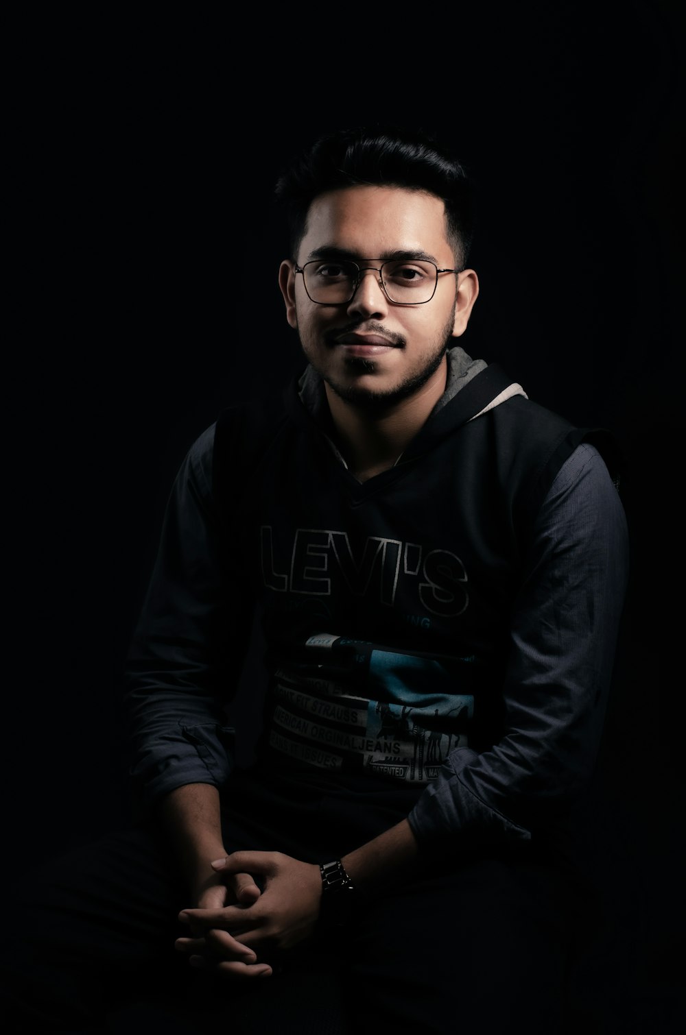 a man with glasses sitting in the dark