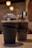 Two large plastic cups with dome lids filled with blended chocolate drinks and topped with whipped cream and chocolate sprinkles. The background is softly lit with warm overhead lights adding a cozy ambiance.