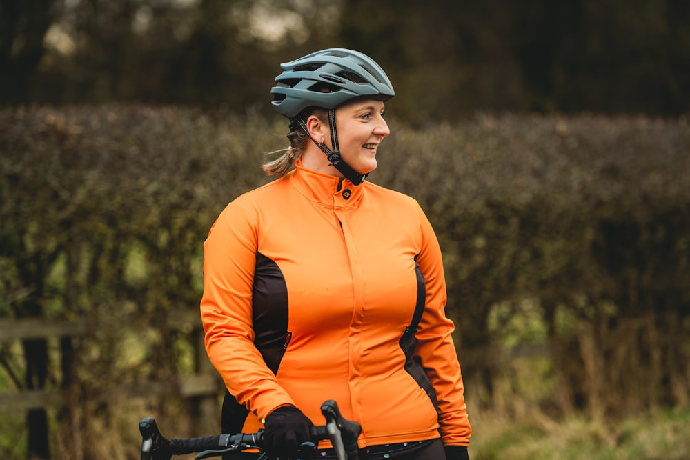 a woman in an orange jacket with a bike helmet
