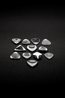 A collection of black and metallic guitar picks laid out on a dark surface showing their unique shapes