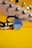 A close-up of a guitar headstock with tuning pegs, accompanied by a black guitar pick and two gold guitar jacks resting on a bright yellow background.