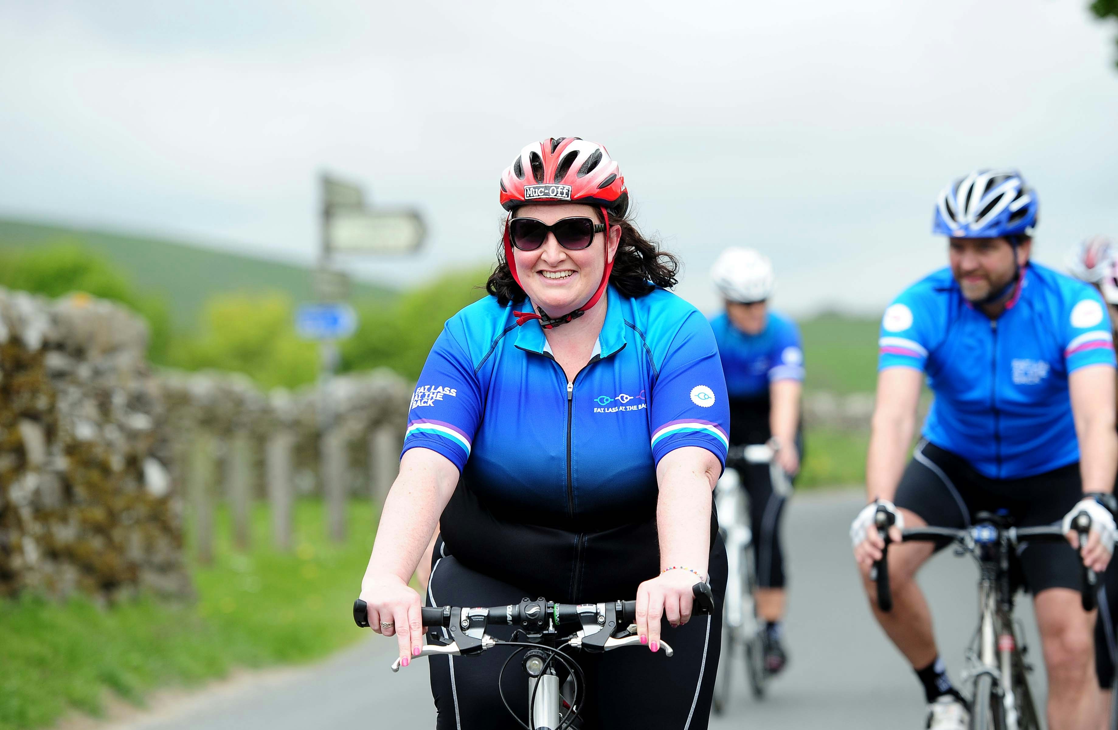 A plus size cyclist smiling riding along a country lane in a blue jersey photographer Simon Wilkinson @swpix.com