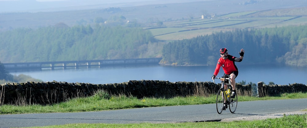 a man riding a bike down a road next to a lush green hillside