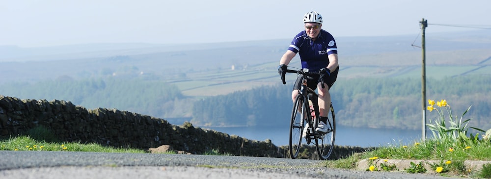 a man riding a bike down a road next to a lush green hillside