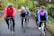 A group of five cyclists are riding on a country road surrounded by lush greenery. They are all wearing helmets and cycling attire, indicating they are on a casual group ride. Their expressions are cheerful, suggesting enjoyment and camaraderie during the activity.