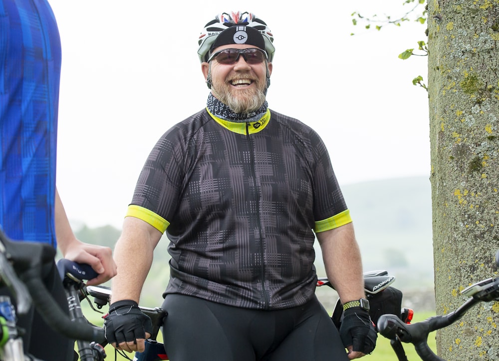 a man wearing a helmet and cycling gear standing next to a tree