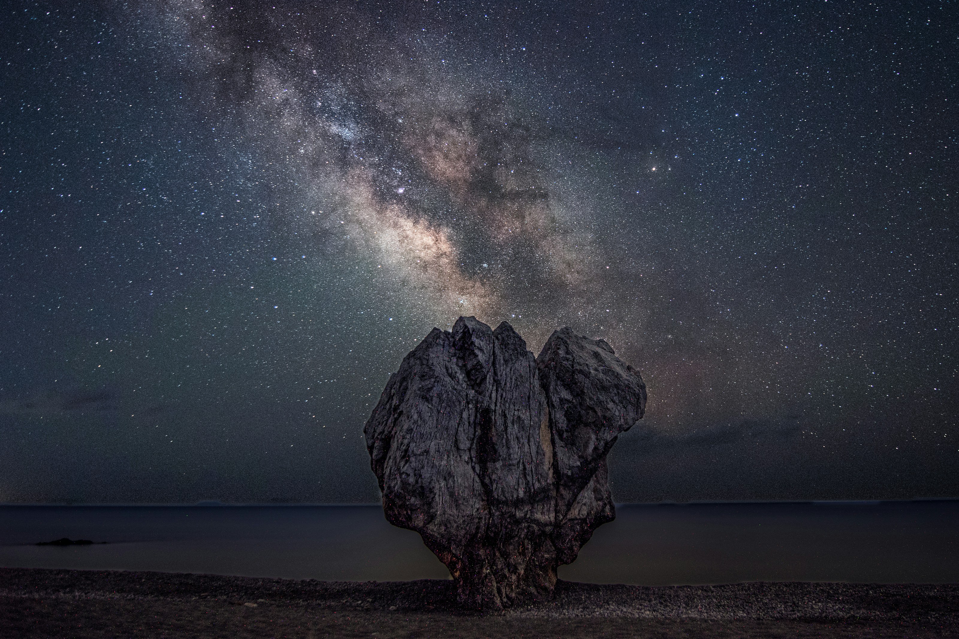 a large rock sitting on top of a beach under a night sky