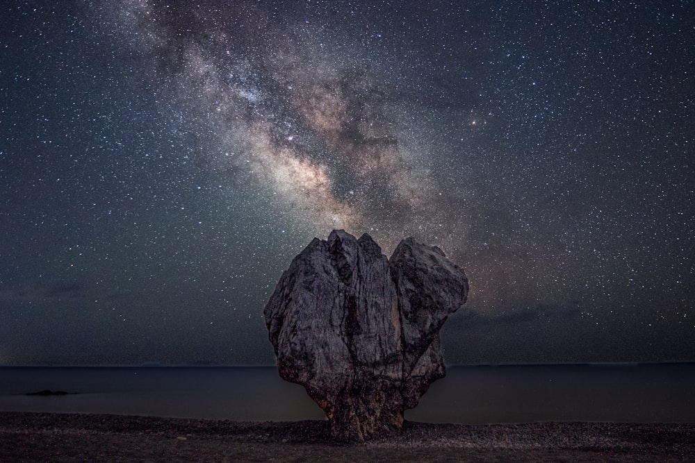 a large rock sitting on top of a beach under a night sky