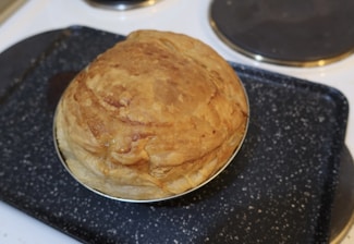 A freshly baked golden brown pie placed on a speckled dark baking tray.