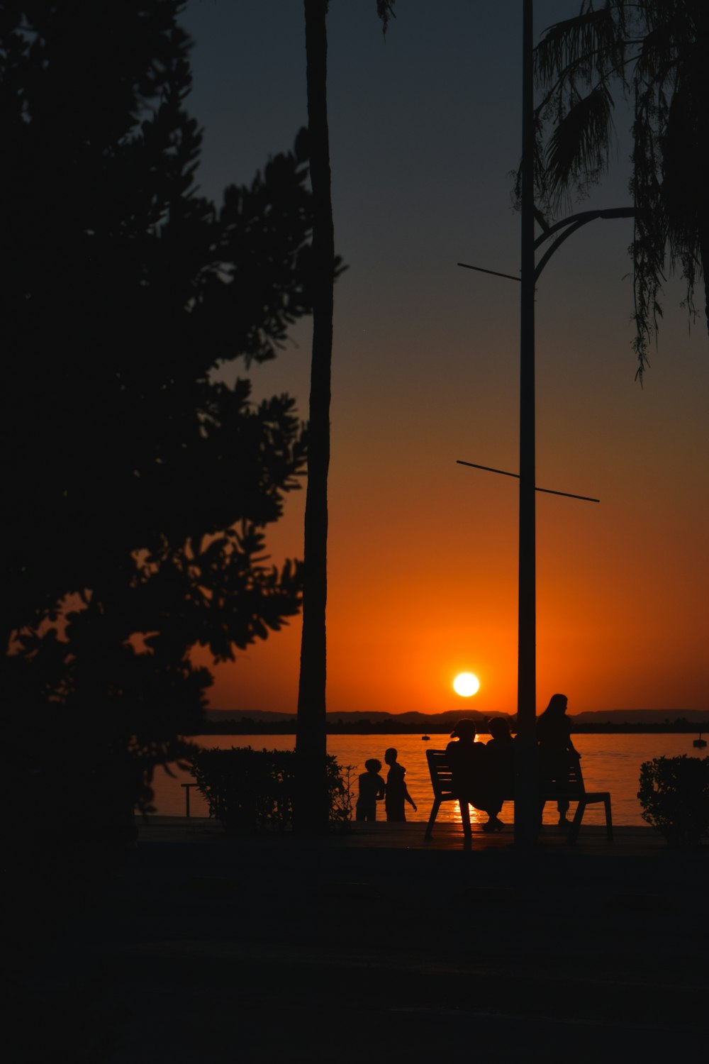 a couple of people sitting on a bench at sunset