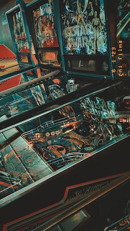 A collection of vintage pinball machines with colorful graphics, including a prominent Star Wars themed game. The machines display intricate designs with various colors and lights, and there is a nostalgic ambiance due to the retro aesthetic.
