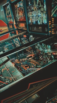 A collection of vintage pinball machines with colorful graphics, including a prominent Star Wars themed game. The machines display intricate designs with various colors and lights, and there is a nostalgic ambiance due to the retro aesthetic.