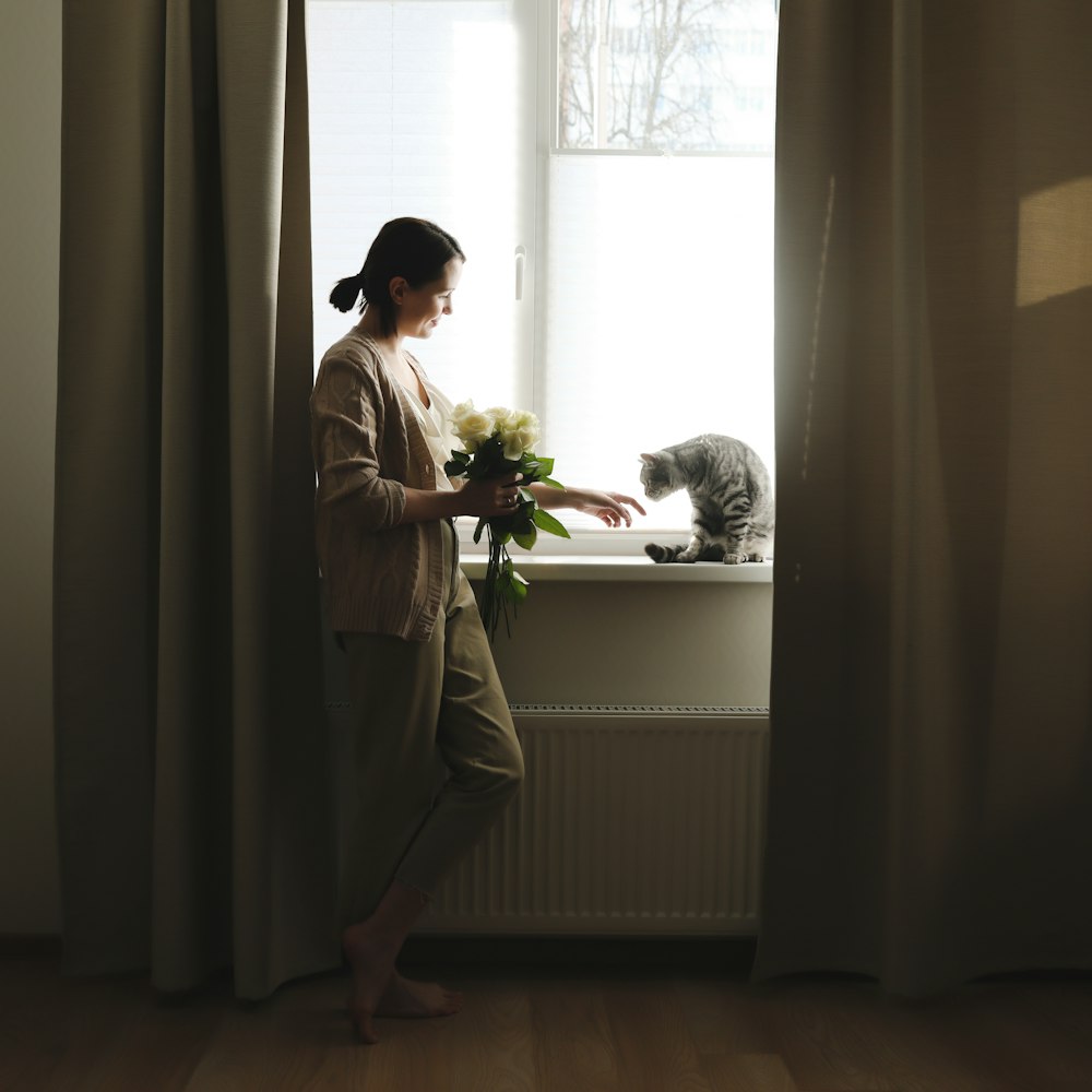 a woman standing in front of a window next to a cat