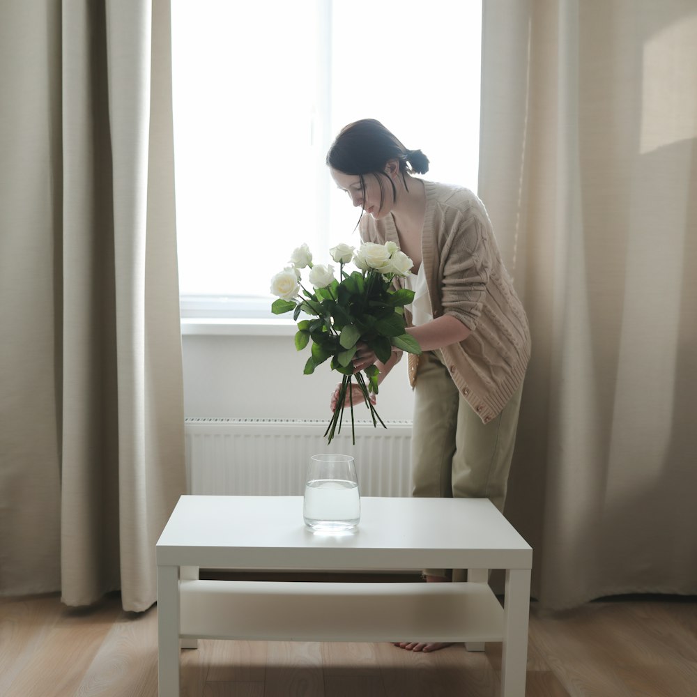 Une femme debout devant une fenêtre tenant un bouquet de fleurs