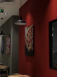An interior view of a restaurant featuring wooden furniture and modern ceiling lights. The walls are adorned with framed pictures of pizza on a rich red background. The atmosphere is cozy with muted lighting.