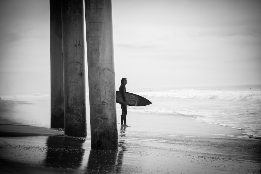 a man holding a surfboard standing under two pillars