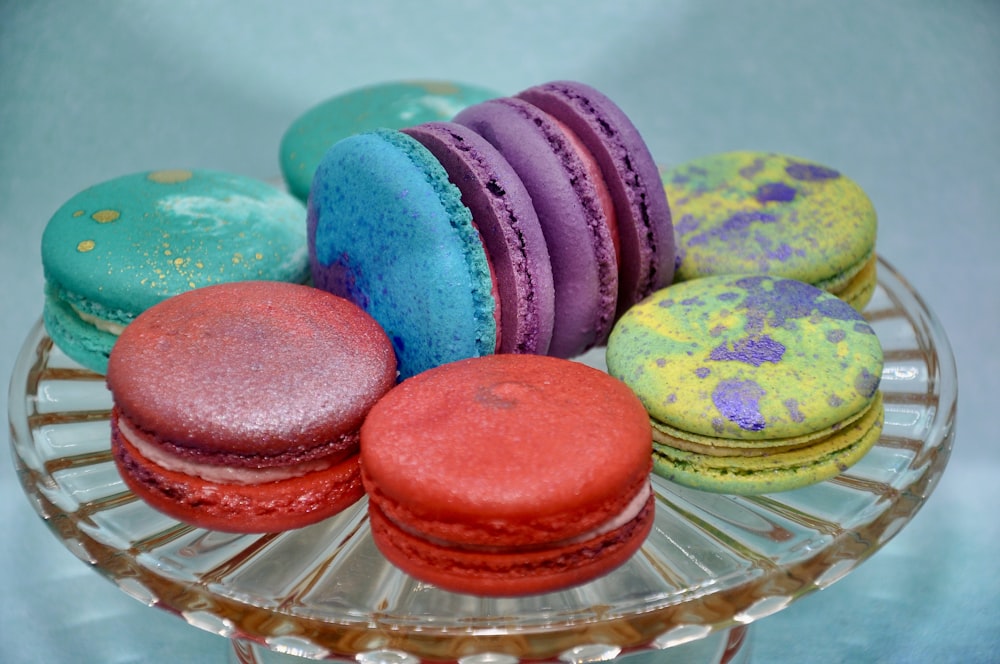 a glass plate filled with colorful macaroons on top of a table