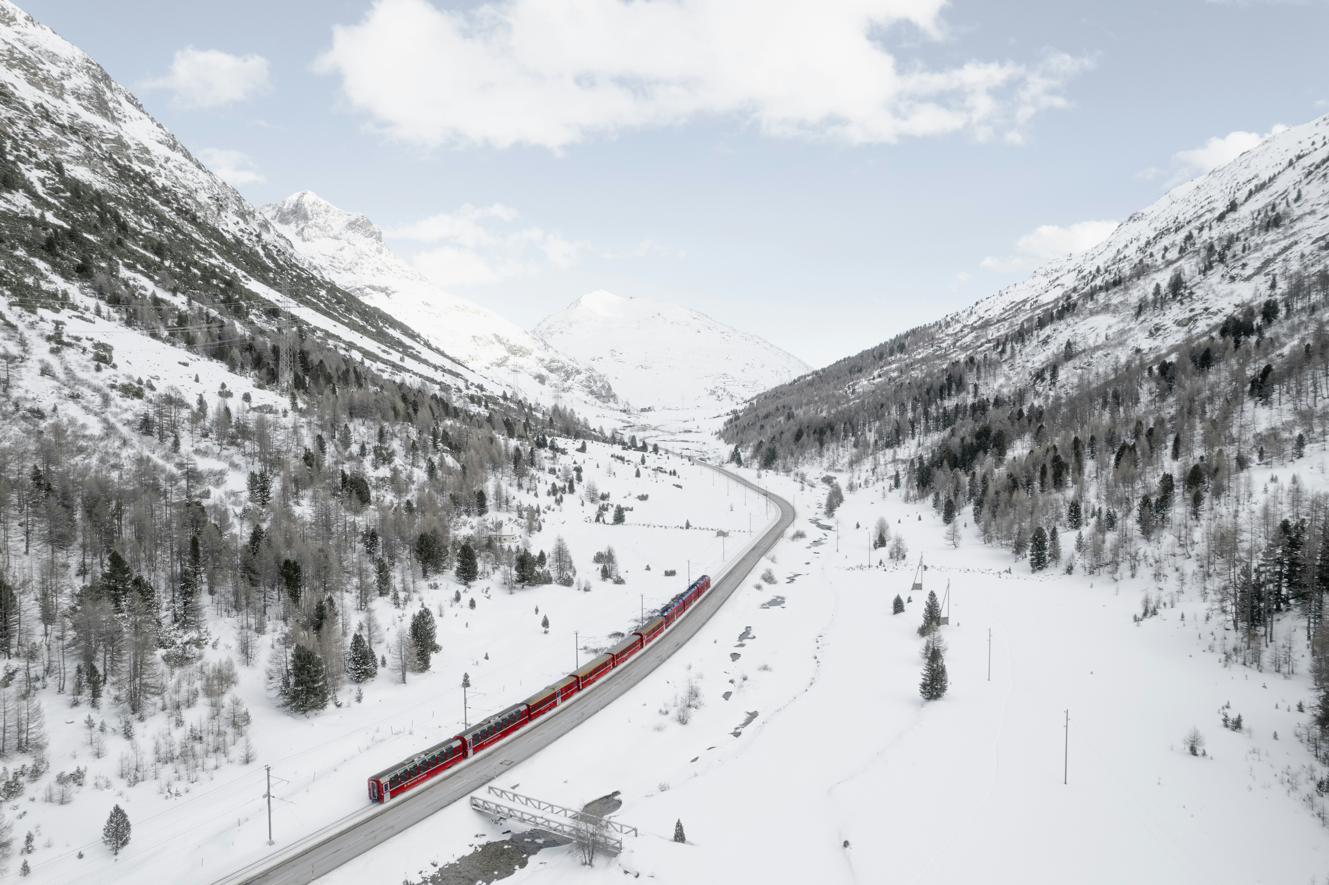 a red train traveling through a snow covered mountain, 