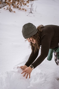 a woman standing in the snow making a snowman