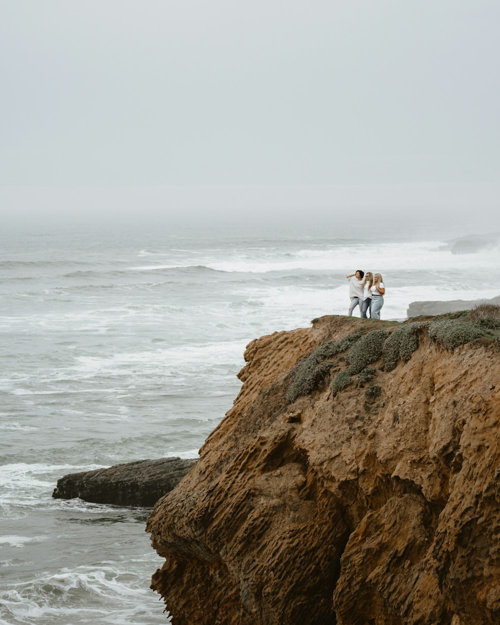 a couple of people standing on top of a cliff next to the ocean