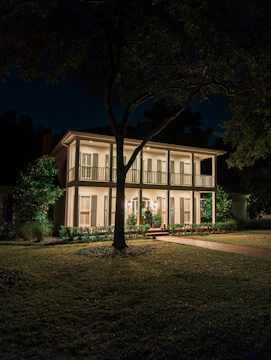 Elegant two-story home with manicured lawn and warm lighting in the evening.
