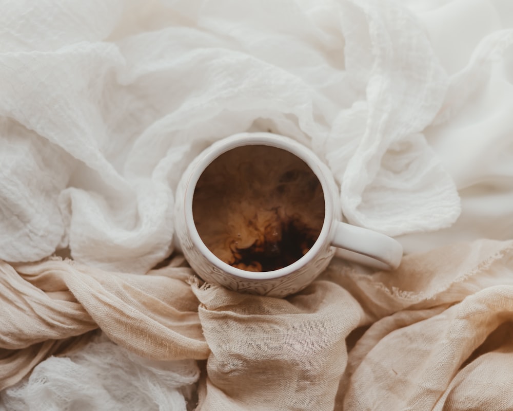 a coffee cup sitting on top of a white blanket
