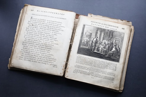 An open antique book featuring pages with text in an old font style on the left and an illustration on the right. The illustration depicts a biblical scene with several figures in a historical setting. The paper appears aged, with yellowed edges and some wear.