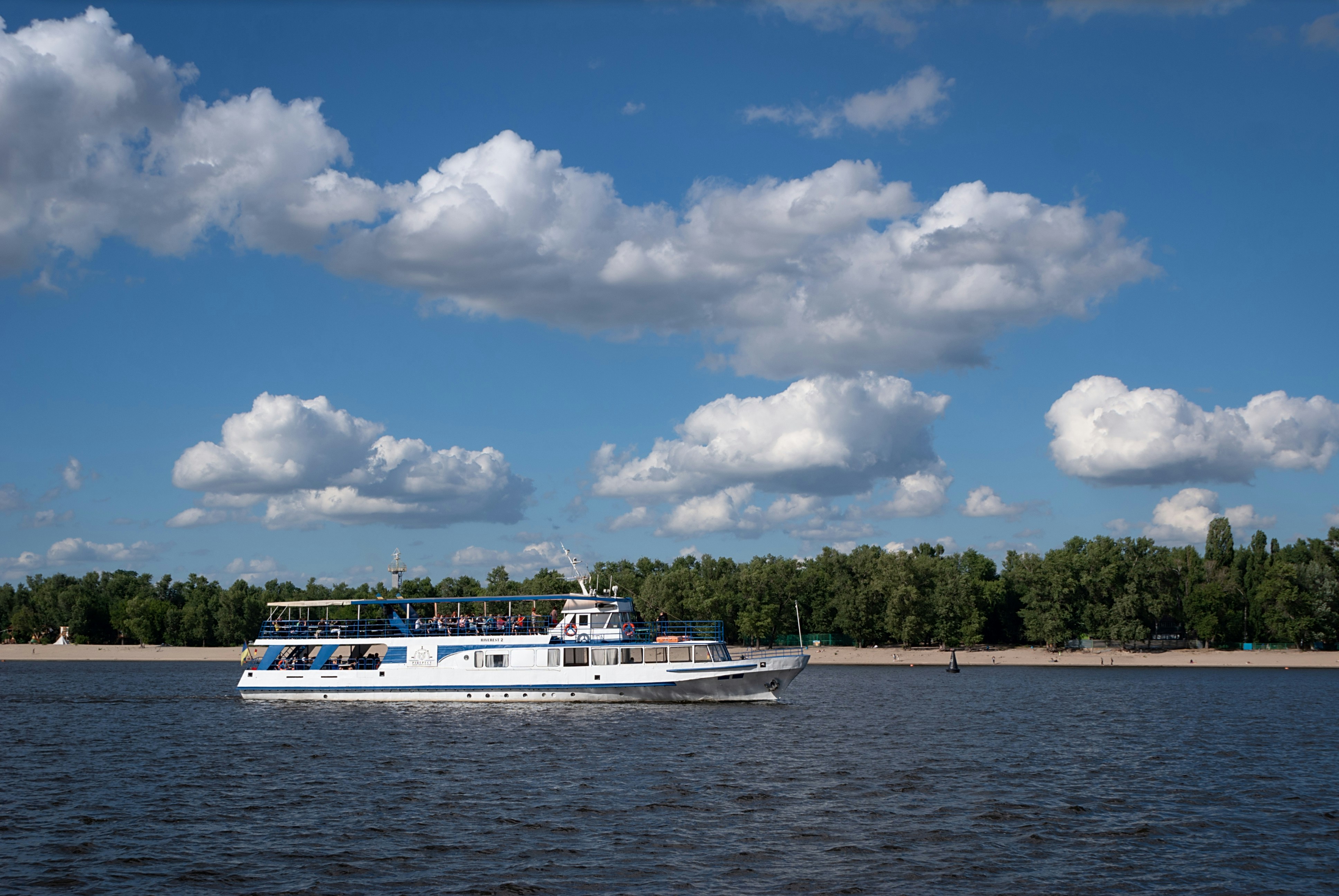 a white boat traveling down a river under a cloudy blue sky