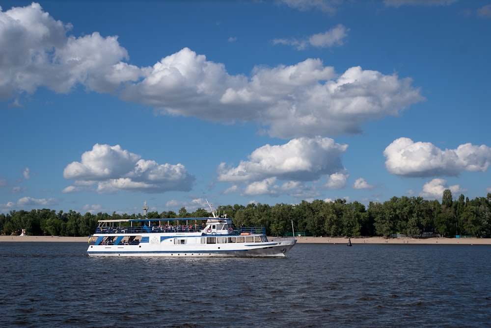 a white boat traveling down a river under a cloudy blue sky