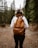 a woman wearing a brown backpack walking through a forest