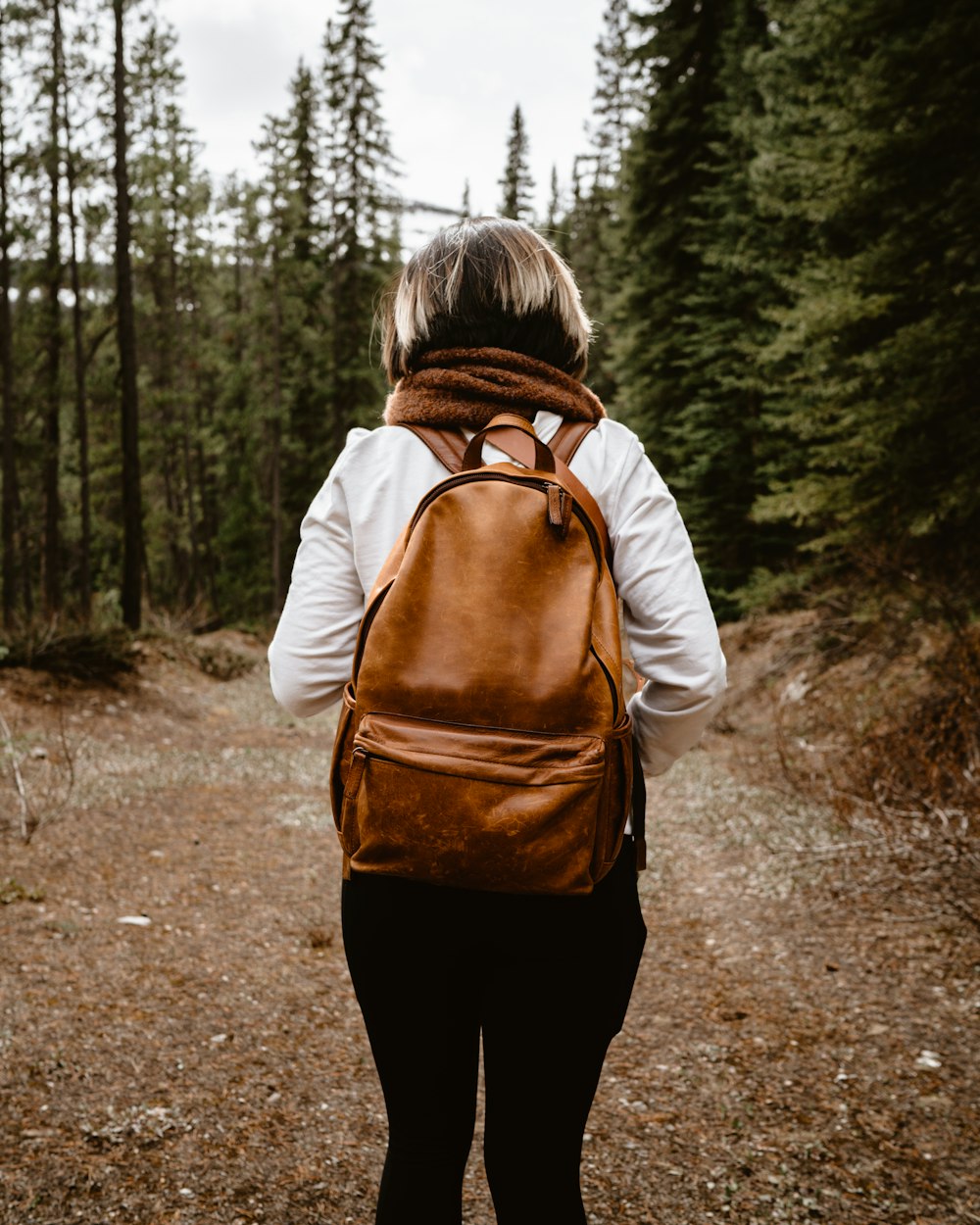 a woman wearing a brown backpack walking through a forest