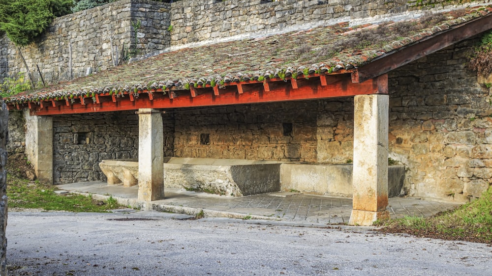 a stone building with a red roof and a bench