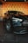 A sleek black car with shiny chrome accents is parked indoors. The car is positioned in front of a wall with repeating 'GA' branding on a warm-toned backdrop. The floor is tiled with large, dark tiles, enhancing the modern vibe of the scene.