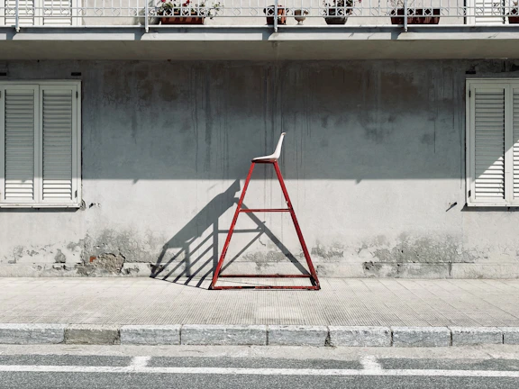 A foldable aluminum step ladder standing beside a fresh coat of paint on a house exterior wall.