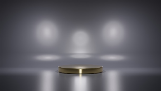 A metallic platform is centered in a minimalistic setting with a reflective surface. Soft, diffused lighting creates circular patterns on the background wall, enhancing the focus on the central stage. The ambiance is sleek and modern, with a hint of elegance.