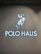 A glowing sign features an illustration of a polo player on a horse, swinging a mallet. Below the image, the words 'POLO HAUS' are illuminated in bright blue neon against a dark background.