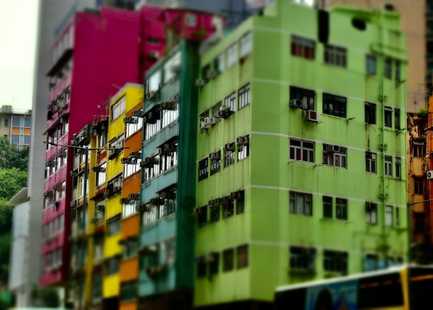 A series of colorful, multi-story apartment buildings with vibrant facades, featuring colors such as green, yellow, orange, and magenta. Each building has numerous windows, some with air conditioning units. The structures appear to be densely packed in an urban setting.