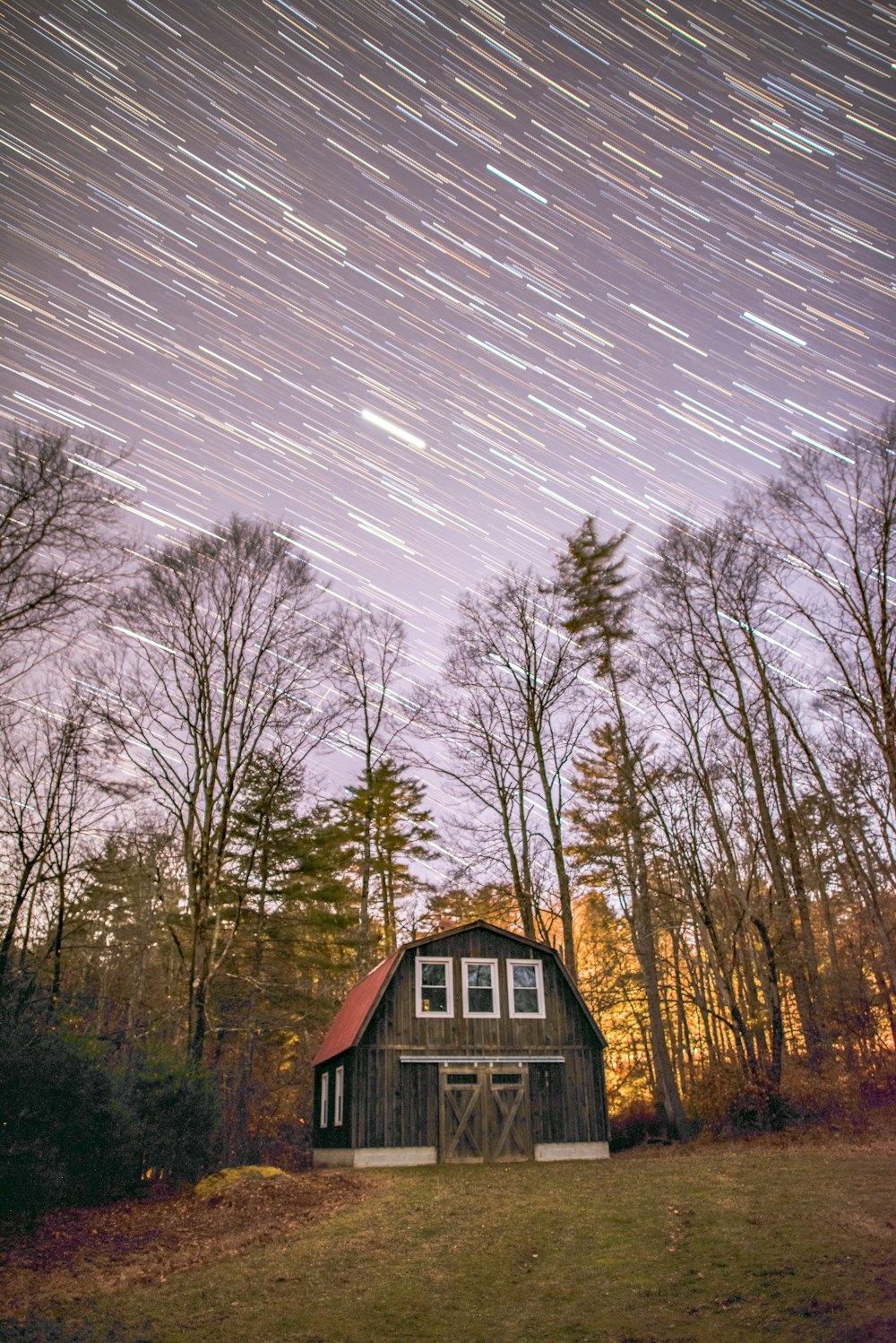 a barn in the woods with a star trail in the sky
