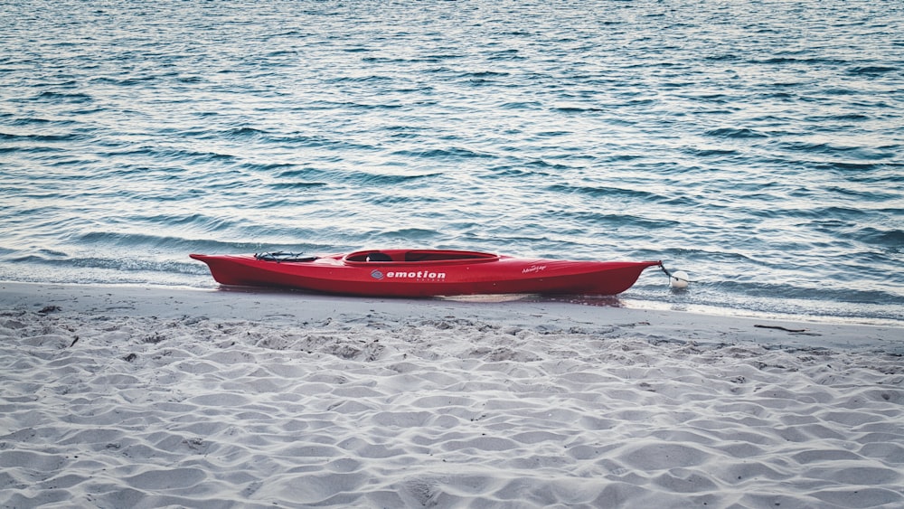 a red boat sitting on top of a sandy beach