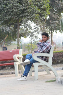 A man casually sitting on a bench wearing a light grey casual shirt, smiling and relaxed.