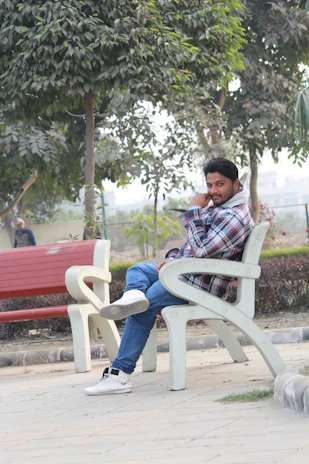 A man casually sitting on a bench wearing a light grey casual shirt, smiling and relaxed.