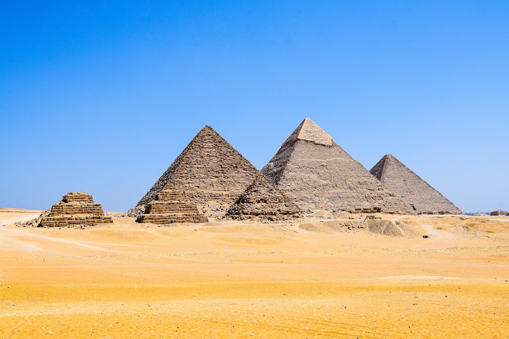 três pirâmides no deserto com um céu azul no fundo