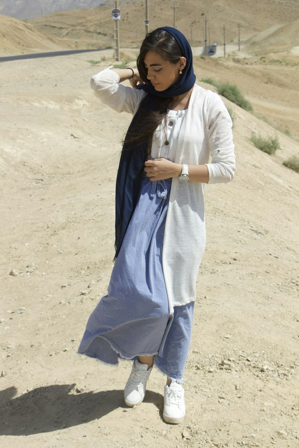 a woman standing on a dirt road wearing a blue dress