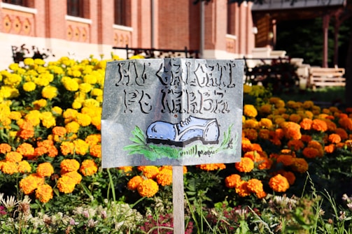 A colorful yard sign planted in fresh green grass outside a small business.