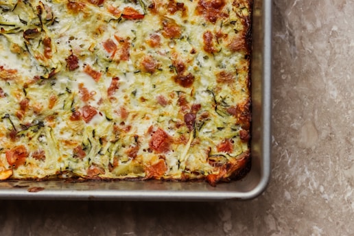 a square casserole dish with cheese and vegetables