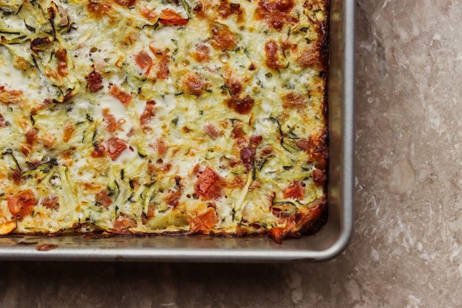 A square casserole dish with melted cheese and baked vegetables