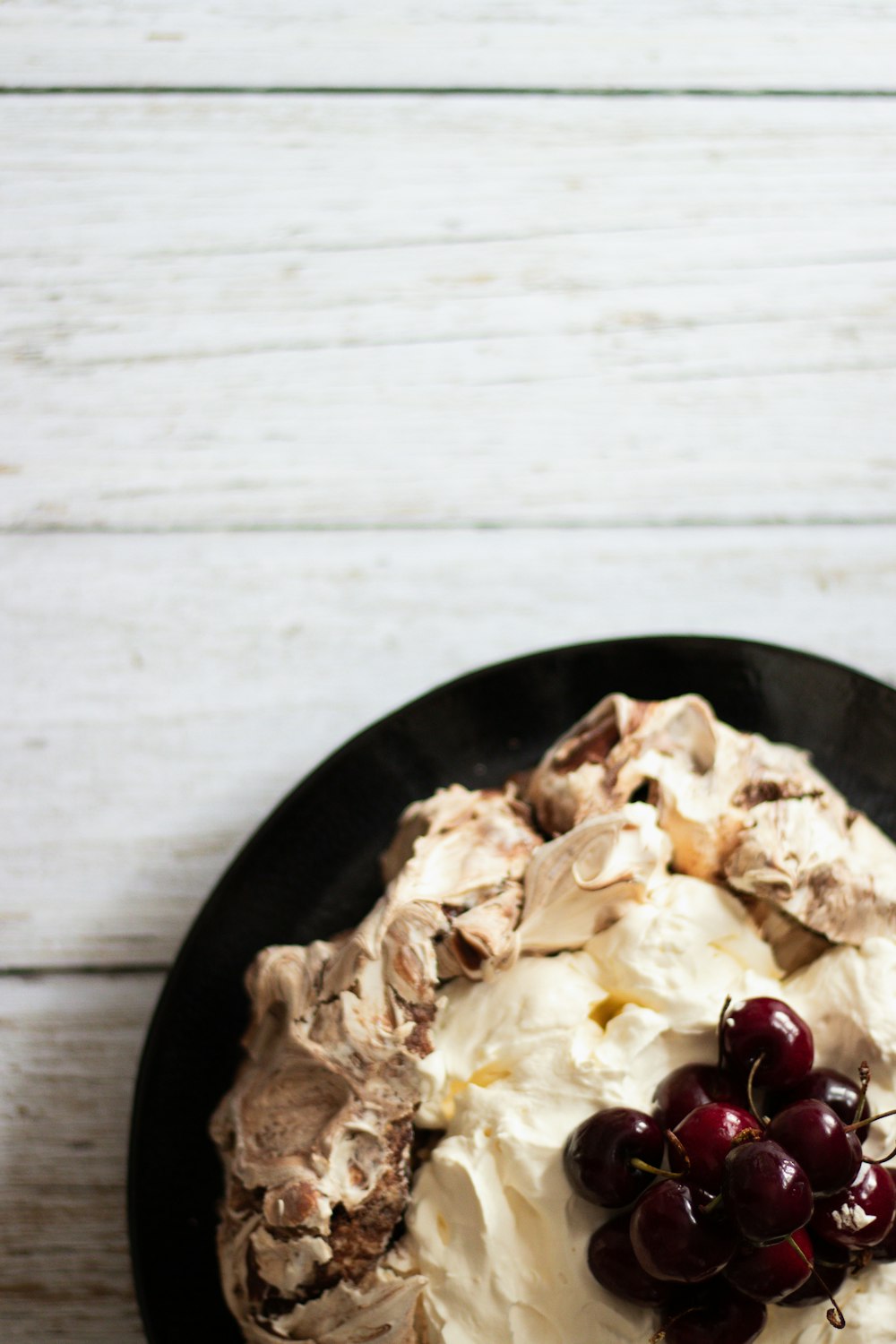 a black plate topped with a cake covered in whipped cream and cherries